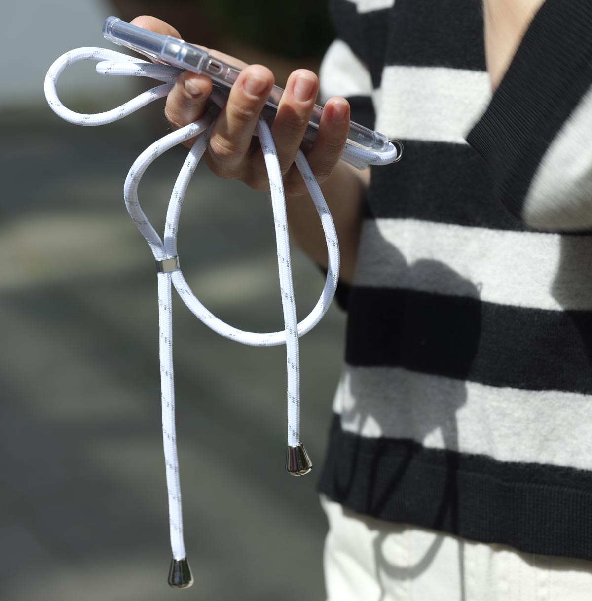 IPhone mit weißer Handykette und silbernen Akzenten wird von einer Frau in der Hand gehalten