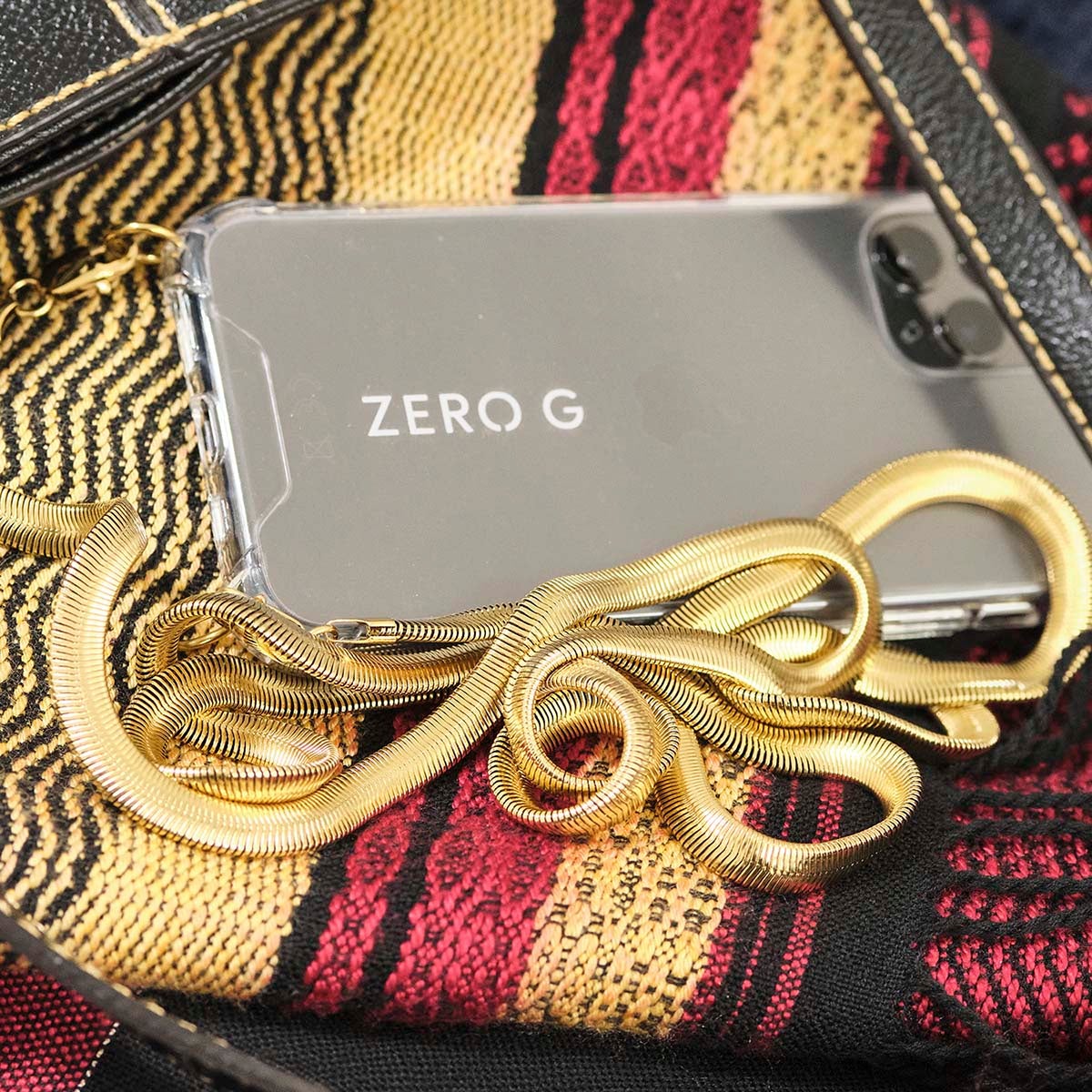 Goldene Metall-Handykette mit Karabinerhäkchen auf buntem Untergrund.