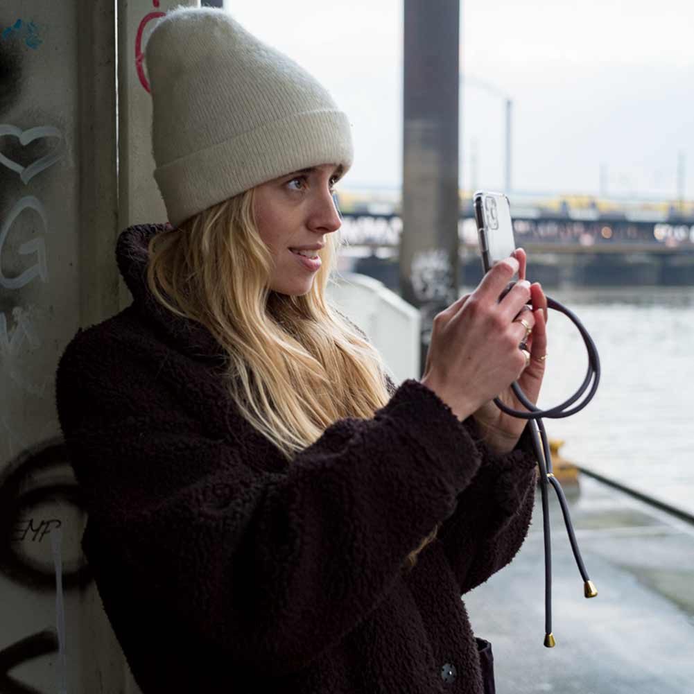 Junge Frau freut sich und macht ein Foto mit Telefon in Handykette mit grauer Schnur