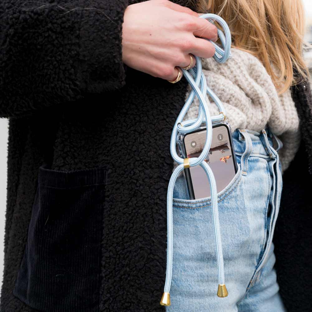 Frau steckt sich Handy mit hellblauer Handykette in die Jeans Hosentasche