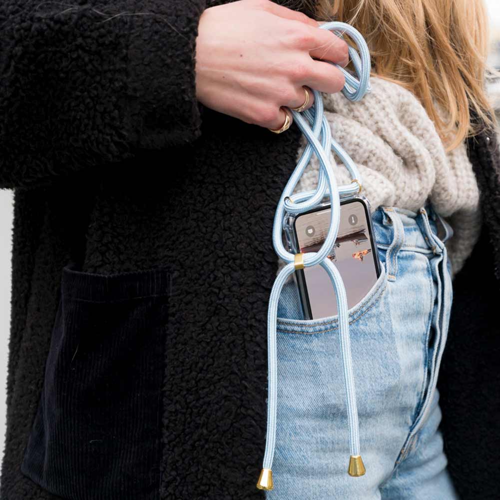 Frau steckt sich Handy mit hellblauer Handykette in die Jeans Hosentasche