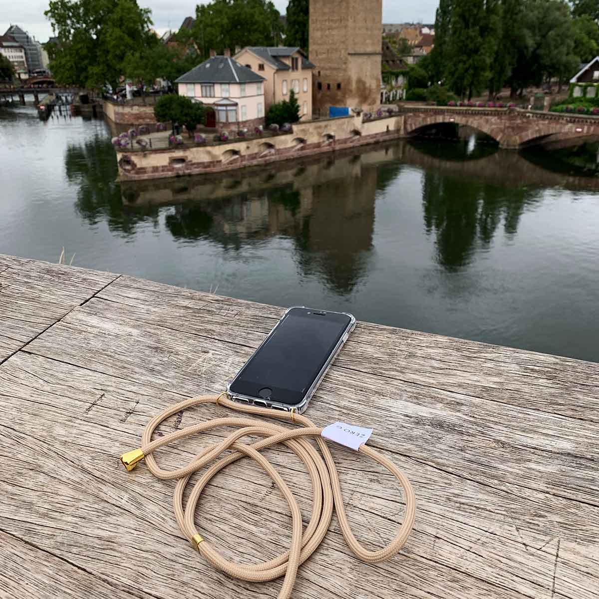 Handyhülle mit beige farbenem Band liegt auf Holz vor schönem Panorama