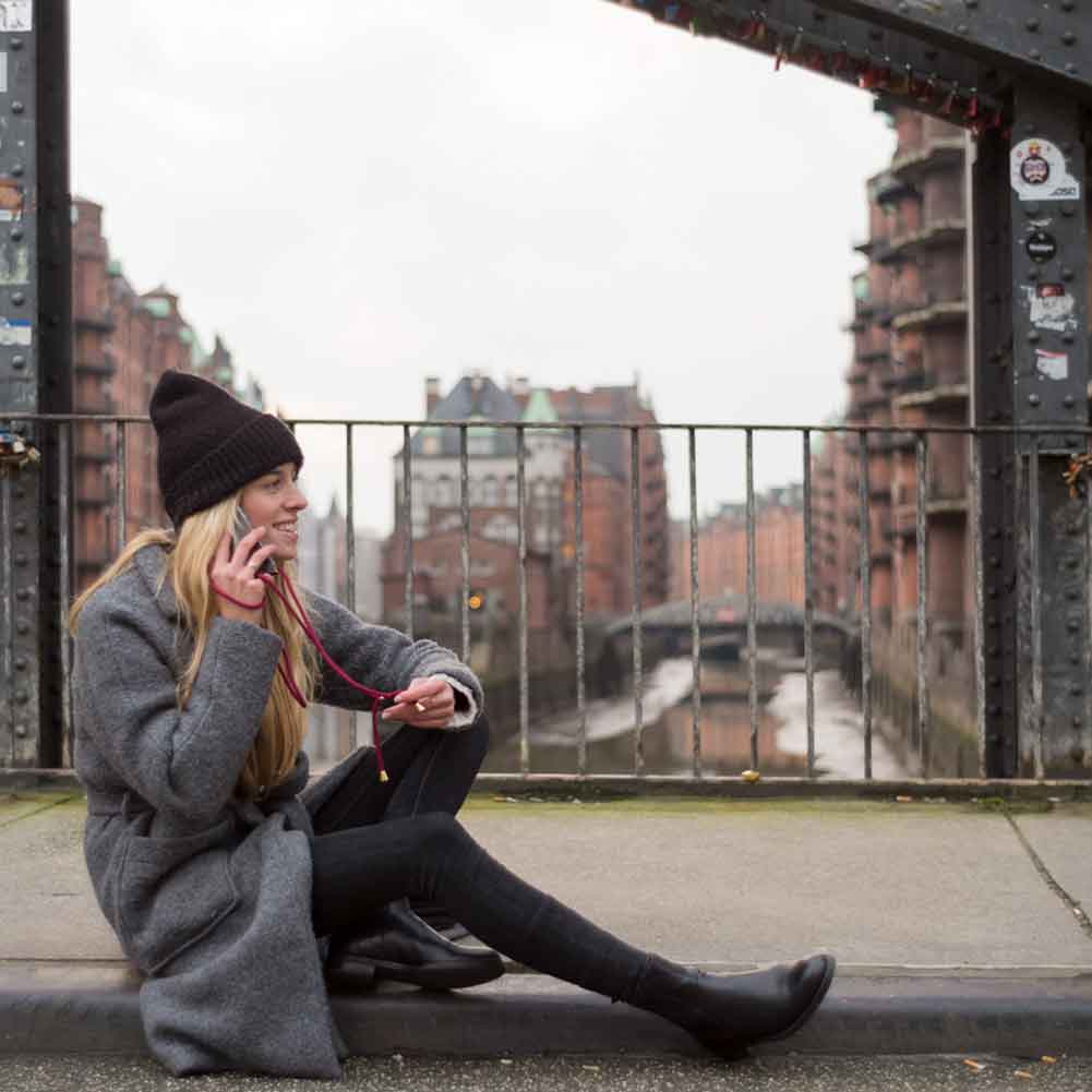 Frau sitzt telefonierend auf Brücke in Speicherstadt und trägt bordeaux Handyband