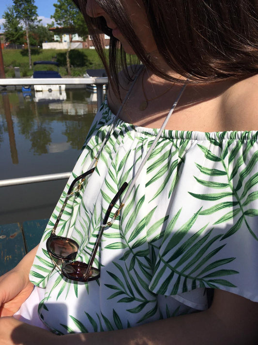Frau trägt hellgraues Brillenband mit befestigter Sonnenbrille um den Hals.